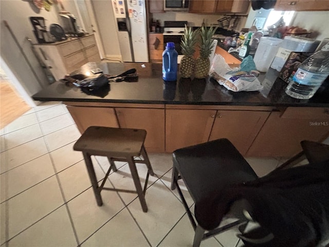 kitchen with range with electric cooktop, a kitchen breakfast bar, light tile patterned floors, and white fridge with ice dispenser