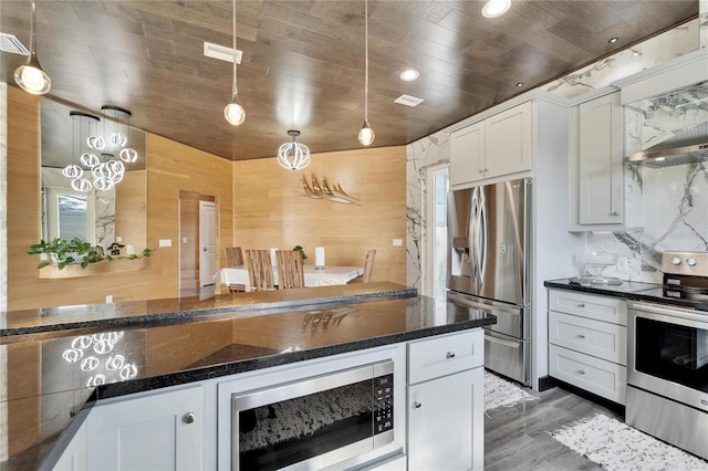 kitchen with white cabinetry, appliances with stainless steel finishes, pendant lighting, and dark stone countertops