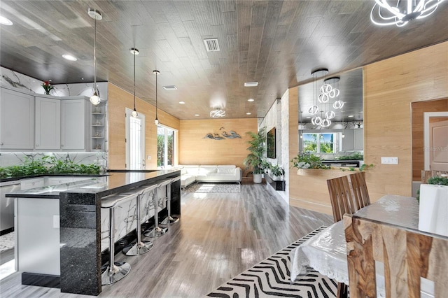 kitchen with white cabinetry, hanging light fixtures, hardwood / wood-style floors, wooden walls, and dark stone counters