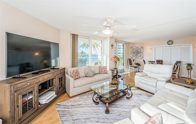 living room featuring ceiling fan, light hardwood / wood-style flooring, and a textured ceiling