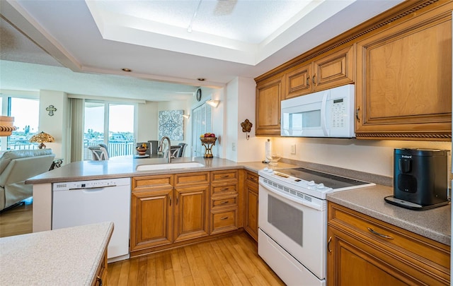 kitchen featuring kitchen peninsula, sink, light hardwood / wood-style floors, a tray ceiling, and white appliances