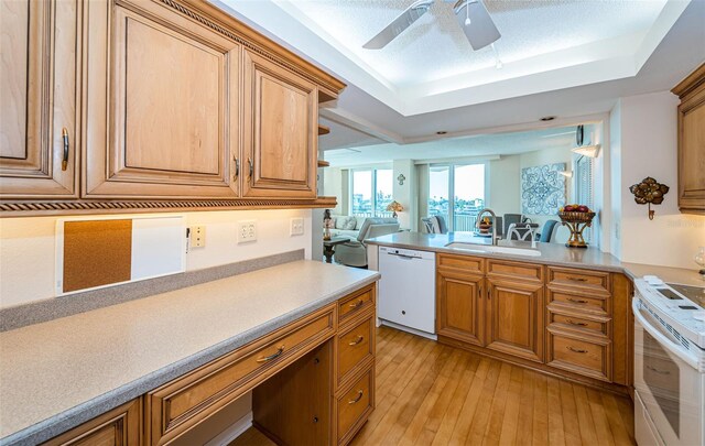 kitchen featuring sink, white appliances, light wood-type flooring, a raised ceiling, and ceiling fan