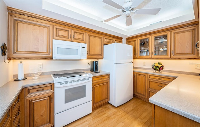 kitchen with ceiling fan, white appliances, a raised ceiling, and light wood-type flooring