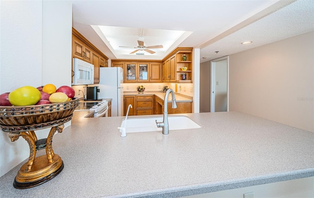 kitchen with sink, white appliances, ceiling fan, a raised ceiling, and kitchen peninsula