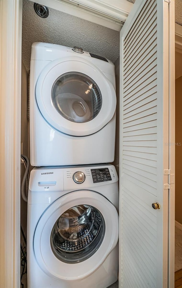 clothes washing area with stacked washer and clothes dryer and a textured ceiling