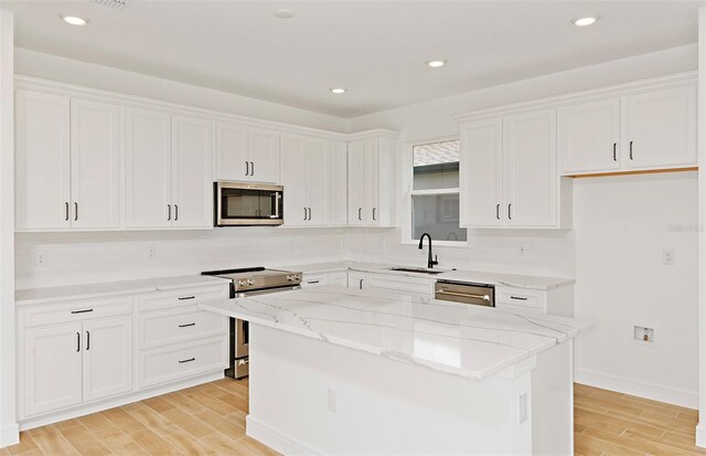 kitchen featuring white cabinets, light stone countertops, a sink, light wood-style flooring, and stainless steel appliances