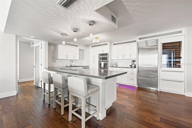 kitchen featuring appliances with stainless steel finishes, white cabinets, dark hardwood / wood-style flooring, decorative light fixtures, and kitchen peninsula