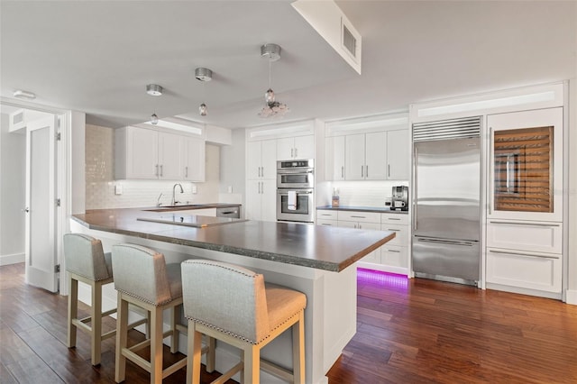 kitchen featuring appliances with stainless steel finishes, dark hardwood / wood-style floors, white cabinetry, a kitchen bar, and kitchen peninsula