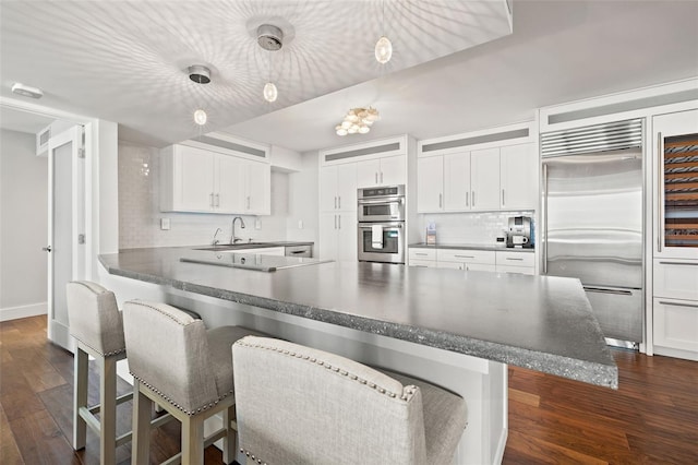 kitchen with white cabinetry, a kitchen breakfast bar, hanging light fixtures, stainless steel appliances, and dark wood-type flooring