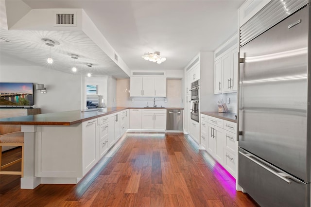 kitchen with appliances with stainless steel finishes, dark hardwood / wood-style flooring, kitchen peninsula, pendant lighting, and white cabinets