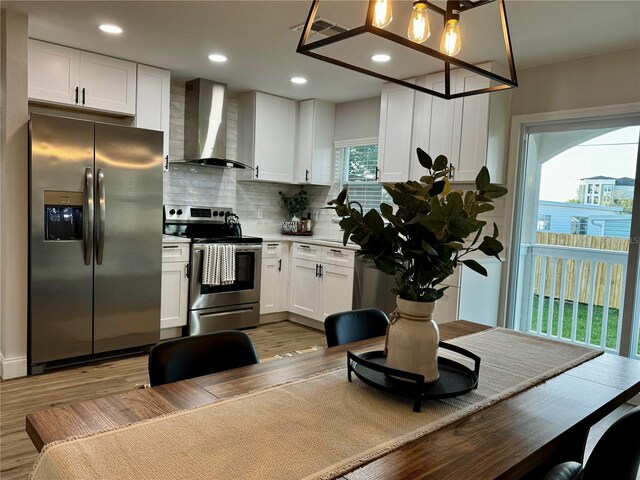 kitchen with white cabinetry, decorative light fixtures, wall chimney exhaust hood, and appliances with stainless steel finishes