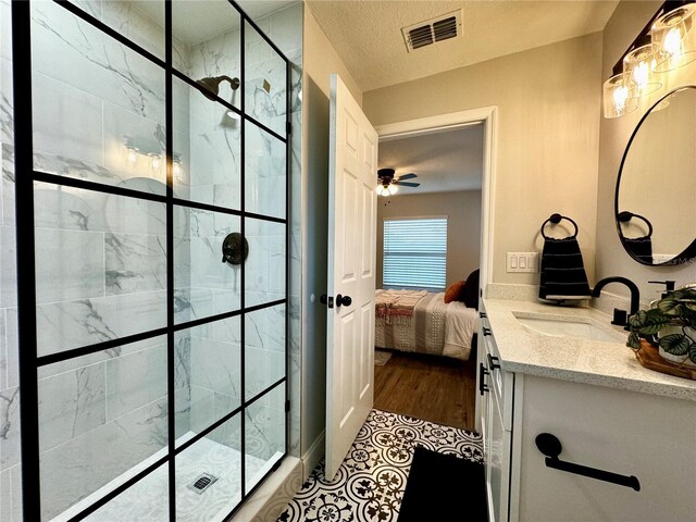bathroom with ceiling fan, vanity, a textured ceiling, and a tile shower