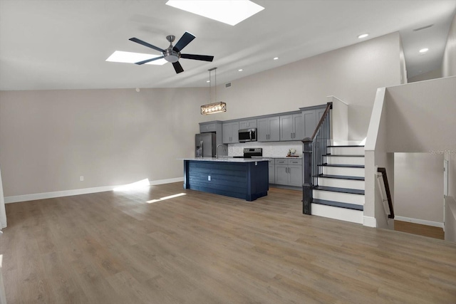 kitchen with ceiling fan, hanging light fixtures, a skylight, stainless steel appliances, and an island with sink