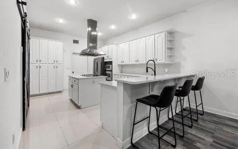 kitchen with a breakfast bar, kitchen peninsula, a kitchen island, island exhaust hood, and white cabinets