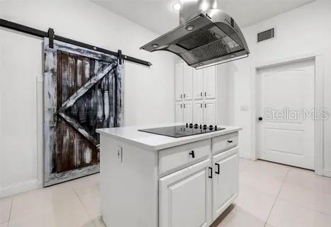 kitchen featuring light tile patterned floors, white cabinetry, a barn door, black electric cooktop, and exhaust hood