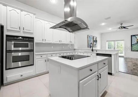 kitchen with a center island, kitchen peninsula, island exhaust hood, stainless steel appliances, and white cabinets