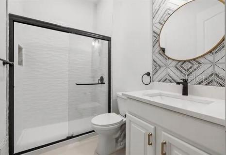 bathroom featuring tasteful backsplash, vanity, toilet, and a shower with door