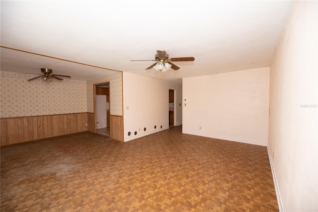 empty room featuring wallpapered walls, ceiling fan, wooden walls, and wainscoting