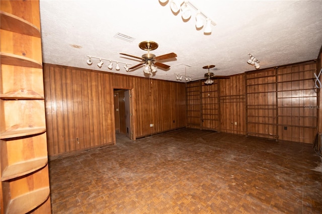 empty room featuring wooden walls, visible vents, a ceiling fan, a textured ceiling, and track lighting