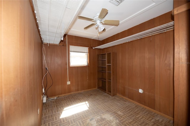 empty room with wooden walls, baseboards, visible vents, a ceiling fan, and parquet floors