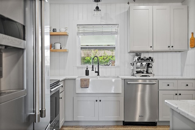 kitchen featuring sink, appliances with stainless steel finishes, white cabinetry, hanging light fixtures, and light stone countertops