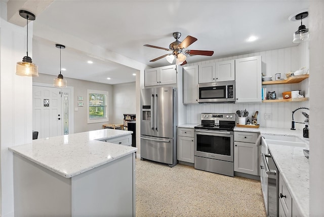 kitchen with sink, hanging light fixtures, a kitchen island, stainless steel appliances, and light stone countertops