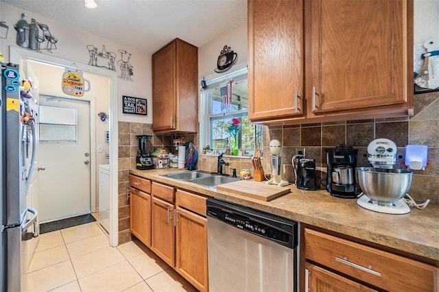 kitchen featuring light tile patterned flooring, appliances with stainless steel finishes, tasteful backsplash, washer / dryer, and sink