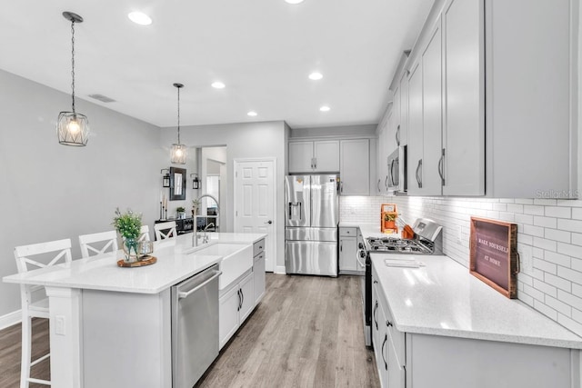 kitchen with hanging light fixtures, stainless steel appliances, a breakfast bar, and a center island with sink