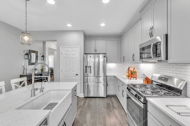 kitchen featuring light stone countertops, appliances with stainless steel finishes, sink, and pendant lighting