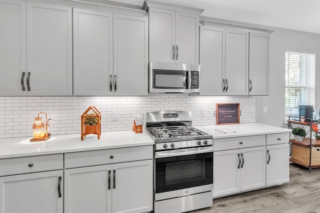 kitchen with stainless steel appliances, light stone countertops, light hardwood / wood-style floors, and backsplash