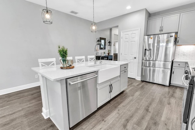 kitchen featuring appliances with stainless steel finishes, pendant lighting, tasteful backsplash, wood-type flooring, and a center island with sink