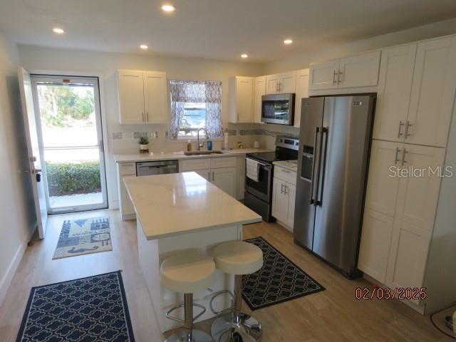 kitchen featuring stainless steel appliances, a kitchen island, sink, and white cabinets