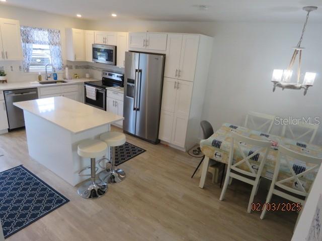 kitchen featuring sink, white cabinetry, stainless steel appliances, a kitchen island, and decorative light fixtures