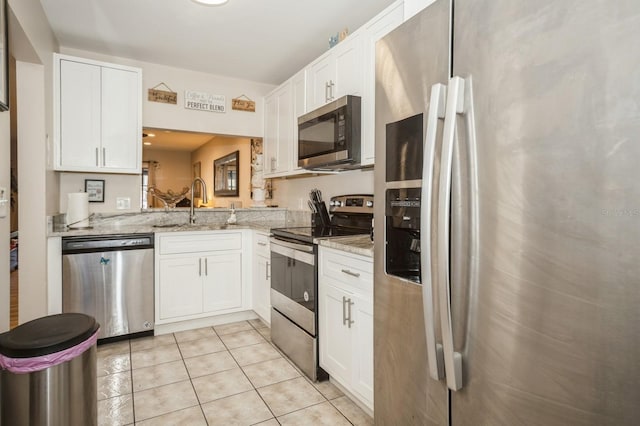 kitchen featuring light tile patterned floors, appliances with stainless steel finishes, light stone counters, white cabinetry, and a sink