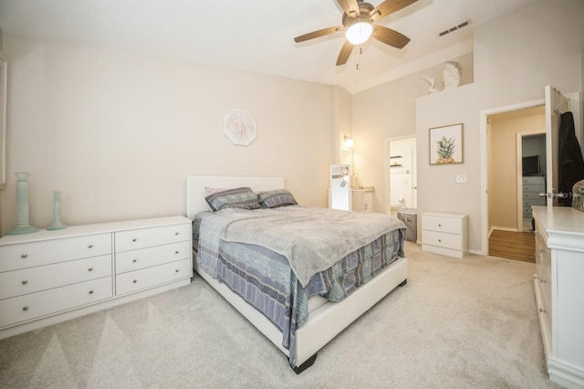 bedroom featuring light colored carpet, visible vents, a ceiling fan, vaulted ceiling, and ensuite bath