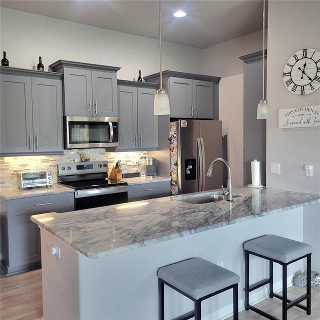 kitchen featuring gray cabinets, sink, hanging light fixtures, stainless steel appliances, and light stone countertops