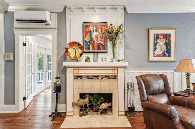 living room with a tile fireplace, wood-type flooring, ornamental molding, french doors, and an AC wall unit