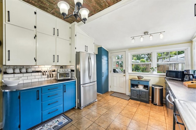 kitchen with light tile patterned floors, appliances with stainless steel finishes, white cabinetry, a notable chandelier, and decorative backsplash