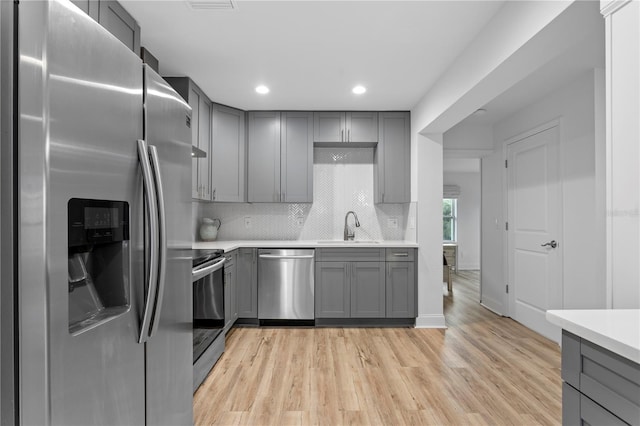 kitchen featuring appliances with stainless steel finishes, a sink, gray cabinets, light countertops, and backsplash