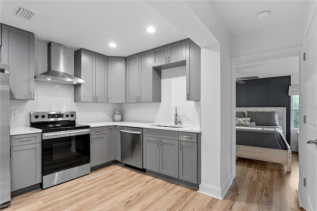 kitchen featuring gray cabinetry, stainless steel appliances, a sink, light countertops, and wall chimney exhaust hood