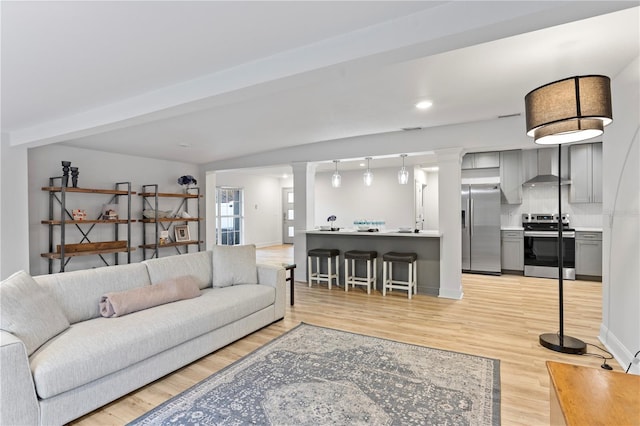 living room featuring recessed lighting, decorative columns, light wood-style flooring, and baseboards