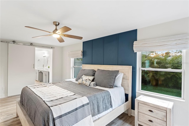 bedroom featuring ceiling fan, a barn door, wood finished floors, and ensuite bathroom