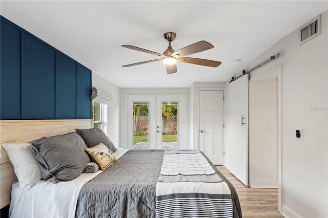 bedroom featuring light wood finished floors, a barn door, visible vents, access to exterior, and french doors