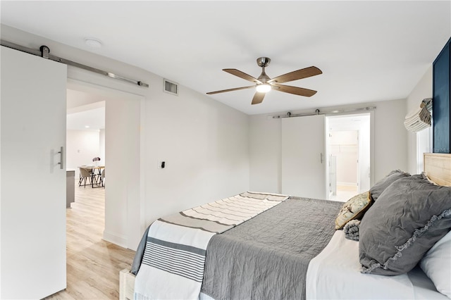 bedroom featuring a ceiling fan, visible vents, light wood-style flooring, and a barn door