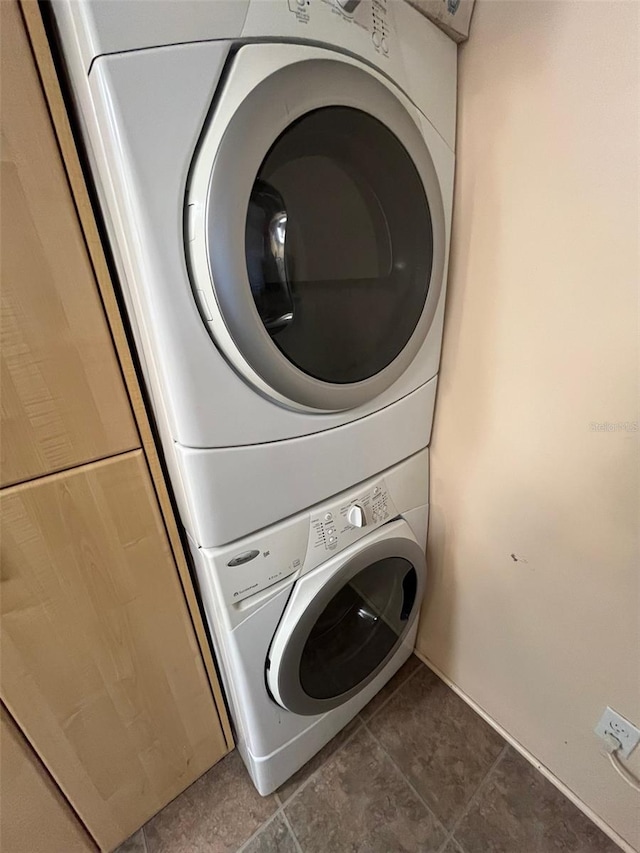 clothes washing area featuring laundry area, dark tile patterned floors, and stacked washer / drying machine