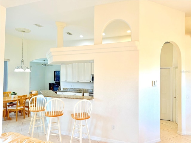 kitchen with a breakfast bar, white cabinets, ceiling fan, kitchen peninsula, and light stone countertops