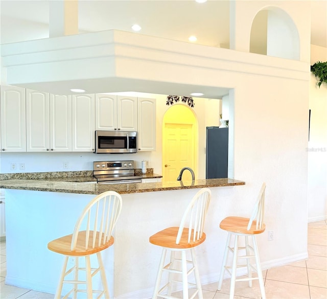 kitchen with white cabinetry, stainless steel appliances, a breakfast bar, and dark stone counters