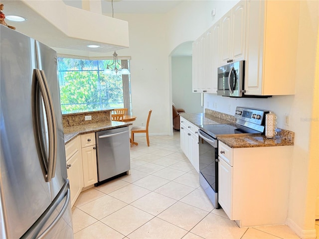 kitchen with hanging light fixtures, stainless steel appliances, dark stone counters, and white cabinets