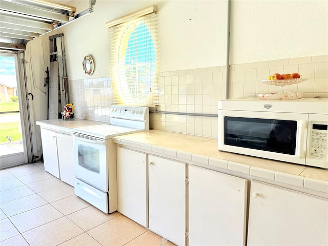 kitchen with white cabinetry, white appliances, a healthy amount of sunlight, and light tile patterned floors