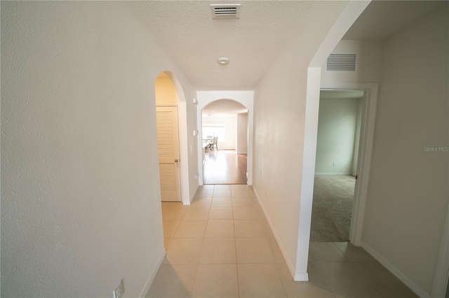 hallway with a textured ceiling and light tile patterned floors